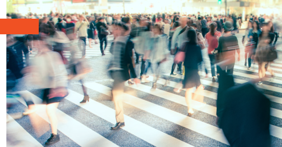 Blurred image of a busy city crosswalk filled with people walking in various directions.