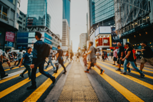 A busy city street with blurred people crossing and tall buildings in the background.