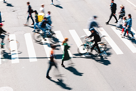 Busy crosswalk with blurred pedestrians and cyclists moving in various directions.
